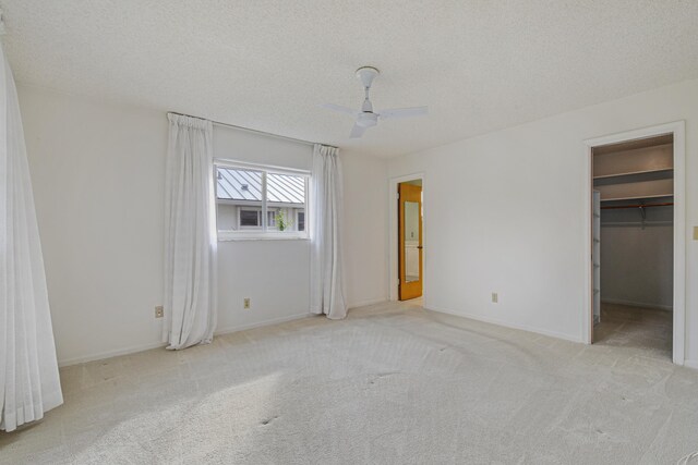 unfurnished bedroom featuring light carpet, ceiling fan, a spacious closet, a textured ceiling, and a closet