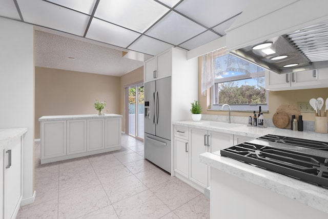 kitchen featuring stainless steel refrigerator with ice dispenser, premium range hood, black gas stovetop, sink, and white cabinetry