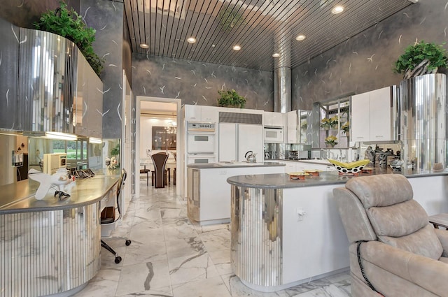 kitchen featuring a high ceiling, kitchen peninsula, white appliances, white cabinets, and wood ceiling