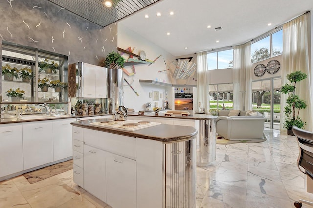 kitchen featuring white cooktop, a kitchen island, white cabinetry, and a high ceiling