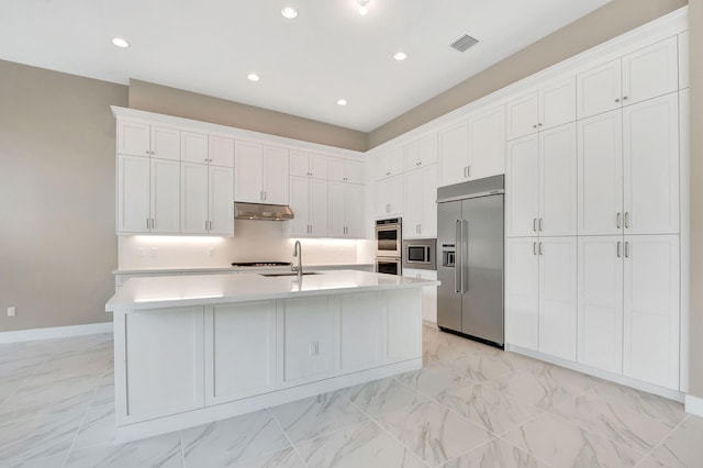 kitchen with built in appliances, a center island with sink, white cabinetry, and sink