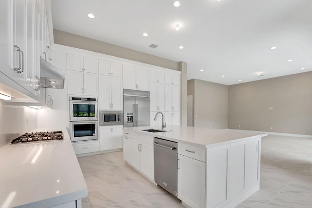 kitchen featuring built in appliances, white cabinets, sink, and an island with sink