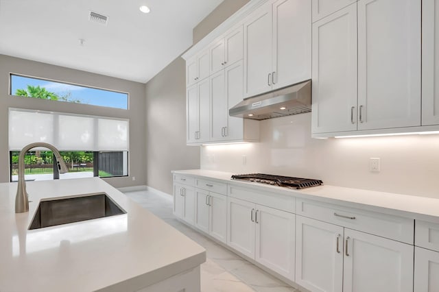 kitchen with white cabinets, stainless steel gas stovetop, decorative backsplash, and sink