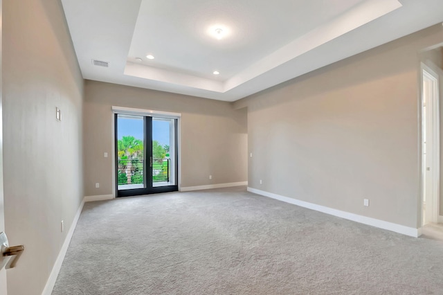 spare room featuring a raised ceiling, french doors, and light colored carpet