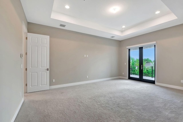 carpeted spare room featuring a raised ceiling and french doors