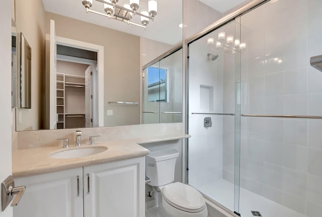 bathroom featuring a notable chandelier, vanity, toilet, and a shower with door