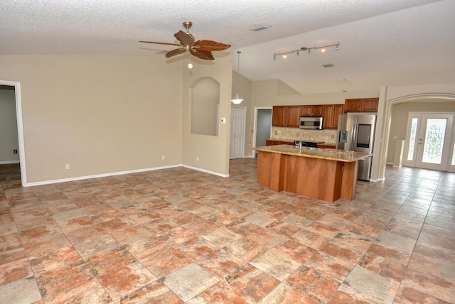 kitchen with appliances with stainless steel finishes, backsplash, a kitchen island with sink, sink, and lofted ceiling