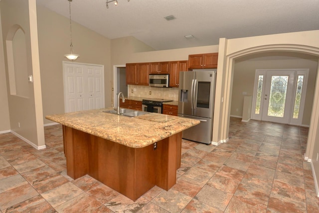 kitchen featuring backsplash, a kitchen island with sink, hanging light fixtures, sink, and stainless steel appliances