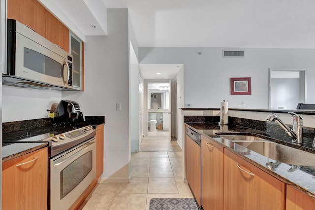 kitchen featuring dark stone counters, sink, light tile patterned floors, and stainless steel appliances