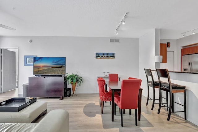 dining room featuring a textured ceiling, rail lighting, and light hardwood / wood-style flooring