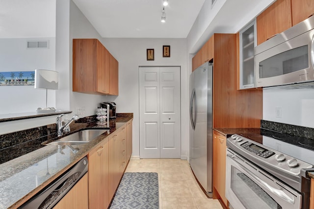 kitchen with light tile patterned flooring, stainless steel appliances, dark stone counters, and sink