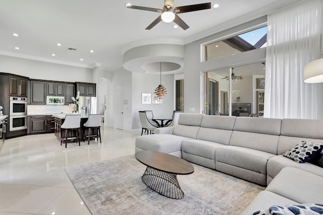 living room featuring a towering ceiling, ceiling fan, crown molding, and light tile patterned floors