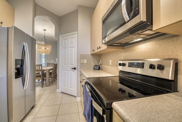 kitchen with light brown cabinets, light tile patterned floors, hanging light fixtures, a chandelier, and appliances with stainless steel finishes