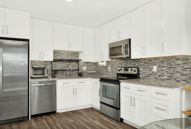 kitchen with light stone countertops, white cabinets, dark hardwood / wood-style floors, and appliances with stainless steel finishes