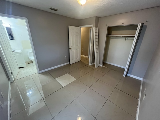 unfurnished bedroom featuring light tile patterned floors, ensuite bath, and a closet