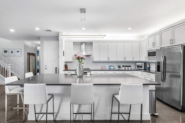 kitchen featuring white cabinets, appliances with stainless steel finishes, a center island, wall chimney exhaust hood, and a breakfast bar