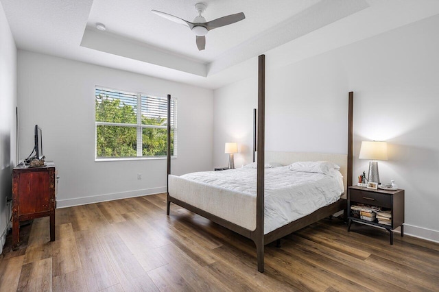 bedroom featuring dark wood-type flooring, ceiling fan, and a tray ceiling