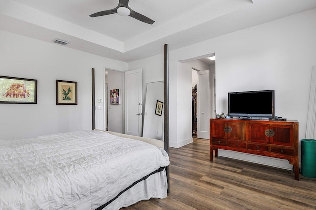 bedroom with ceiling fan, dark hardwood / wood-style flooring, and a tray ceiling