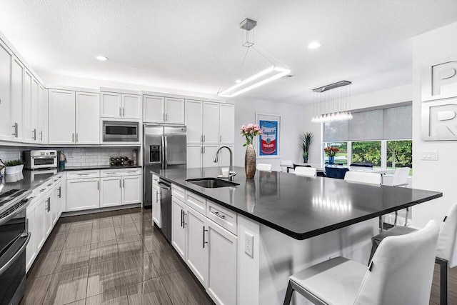 kitchen with hanging light fixtures, sink, stainless steel appliances, and white cabinetry