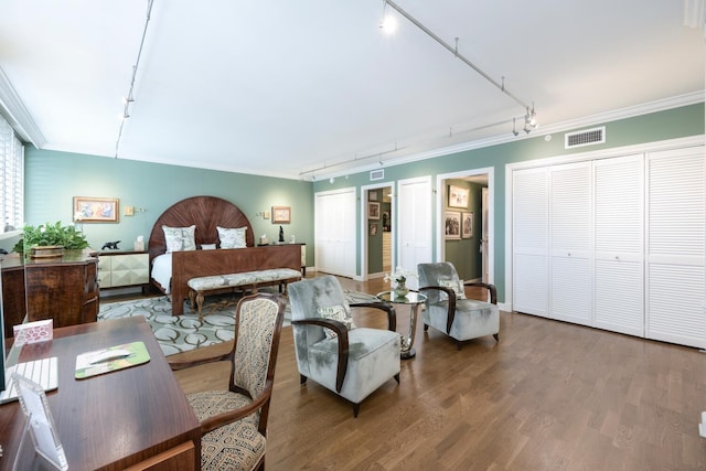 bedroom with a closet, rail lighting, wood-type flooring, and ornamental molding