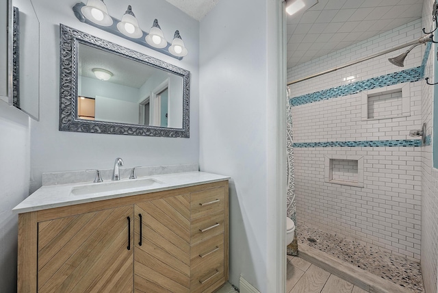 bathroom with a tile shower, vanity, and toilet