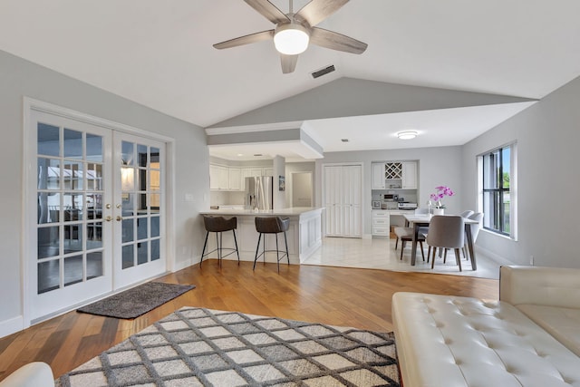 living room featuring ceiling fan, light hardwood / wood-style floors, french doors, and vaulted ceiling