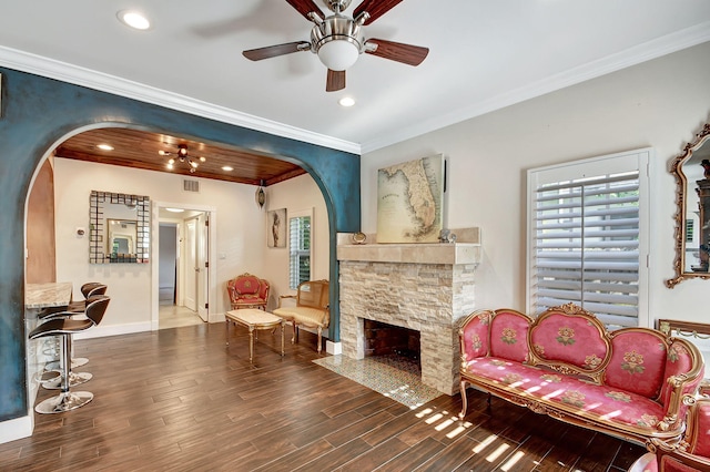 living room featuring ornamental molding, a stone fireplace, ceiling fan, and dark wood-type flooring