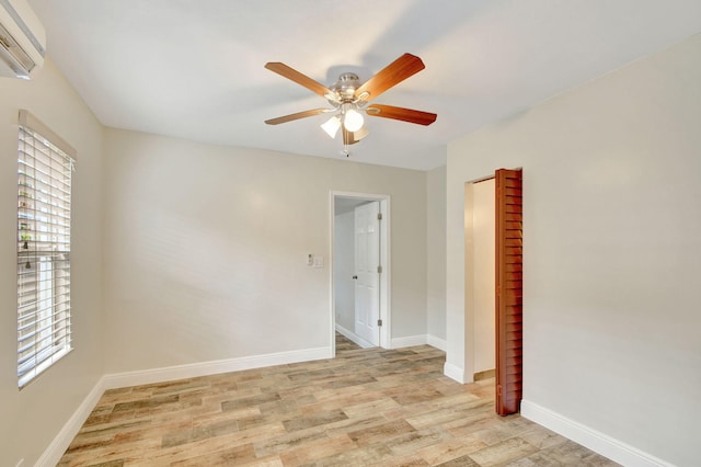 spare room with ceiling fan, an AC wall unit, a wealth of natural light, and light hardwood / wood-style flooring