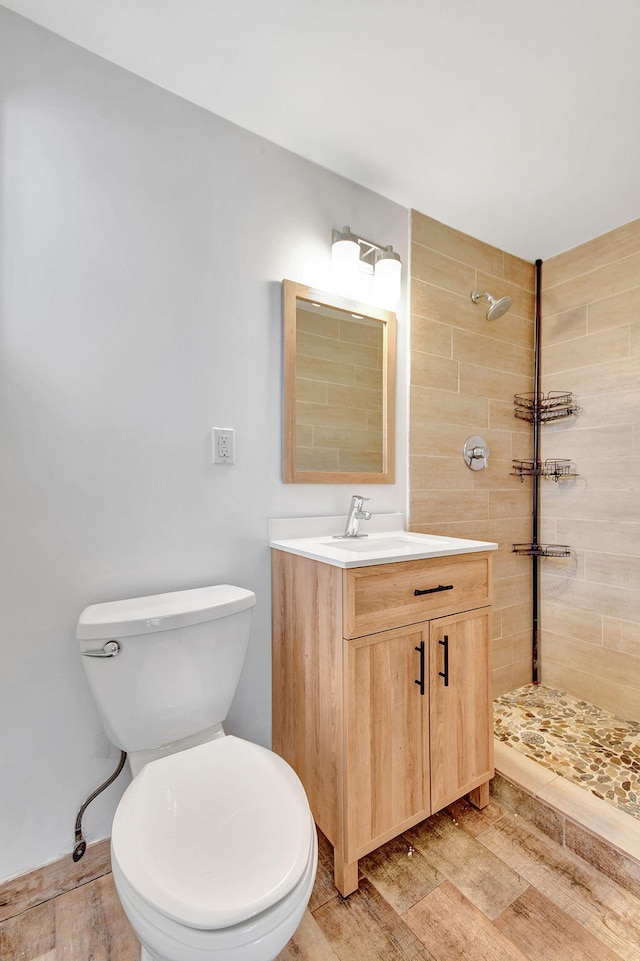 bathroom featuring hardwood / wood-style flooring, vanity, toilet, and tiled shower