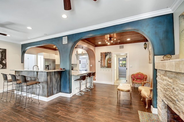 kitchen with ceiling fan, dark wood-type flooring, light stone counters, stainless steel refrigerator with ice dispenser, and ornamental molding