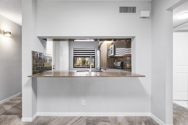 kitchen with stone counters, a textured ceiling, stainless steel appliances, and sink