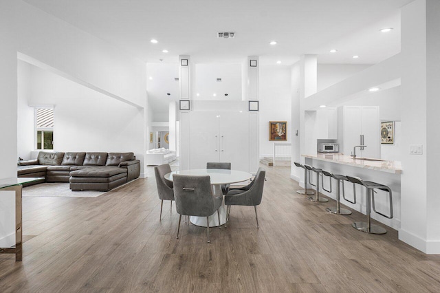 dining space featuring a towering ceiling, light hardwood / wood-style flooring, and sink