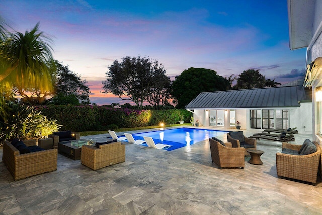 pool at dusk featuring an outbuilding, a patio, and an outdoor living space with a fire pit