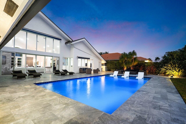 pool at dusk with outdoor lounge area and a patio