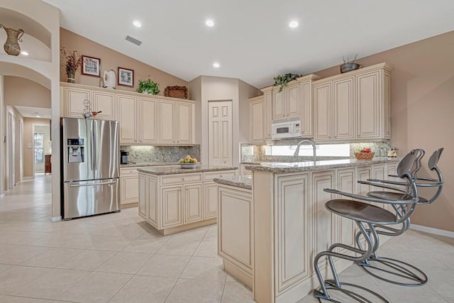 kitchen featuring cream cabinets, a center island, stainless steel refrigerator with ice dispenser, and vaulted ceiling