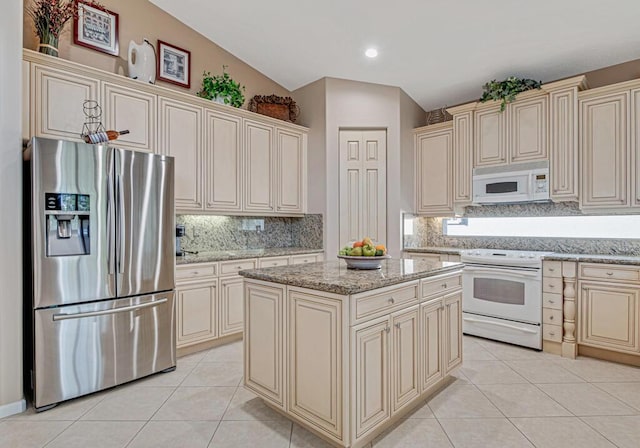 kitchen with light stone countertops, white appliances, vaulted ceiling, cream cabinetry, and a center island