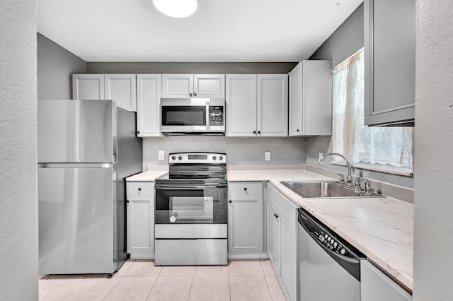 kitchen with light tile patterned floors, stainless steel appliances, light stone counters, and sink