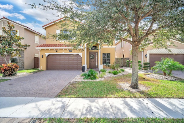 mediterranean / spanish home with fence, stucco siding, a garage, a tiled roof, and decorative driveway