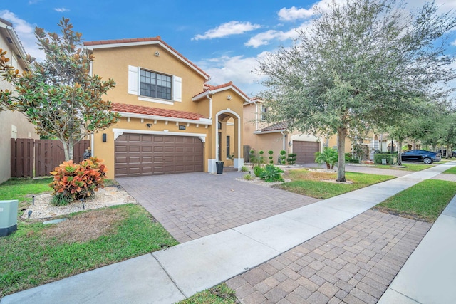 mediterranean / spanish-style house with fence, stucco siding, a garage, a tiled roof, and decorative driveway