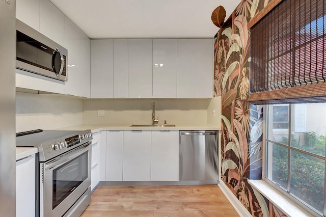 kitchen featuring stainless steel appliances, white cabinetry, plenty of natural light, and light hardwood / wood-style floors