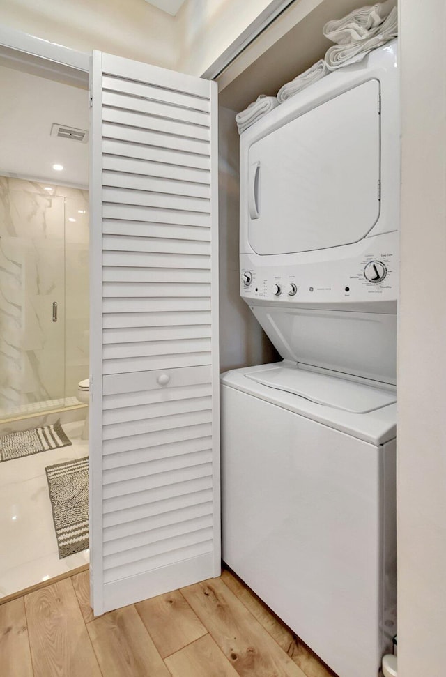 clothes washing area with light hardwood / wood-style floors and stacked washer / drying machine