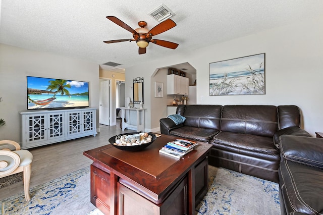 living room with a textured ceiling, light hardwood / wood-style flooring, and ceiling fan