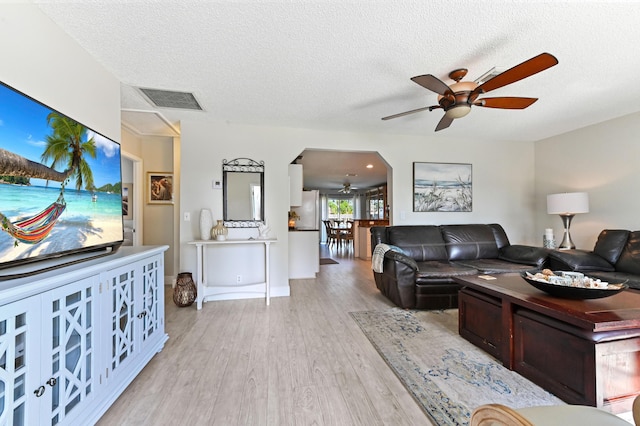 living room featuring ceiling fan, light wood-type flooring, and a textured ceiling