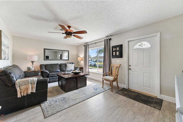 living room featuring ceiling fan, light wood-type flooring, and a textured ceiling