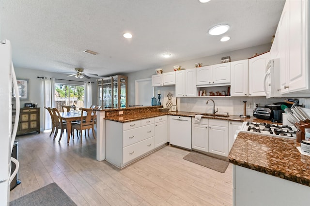 kitchen with kitchen peninsula, white appliances, white cabinetry, and dark stone counters