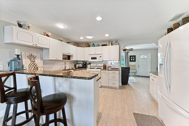 kitchen with a breakfast bar, white appliances, kitchen peninsula, and white cabinets