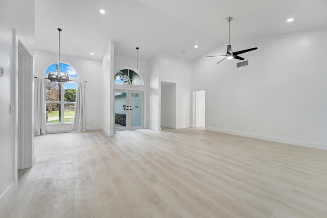 unfurnished living room with french doors, ceiling fan with notable chandelier, light hardwood / wood-style floors, and high vaulted ceiling