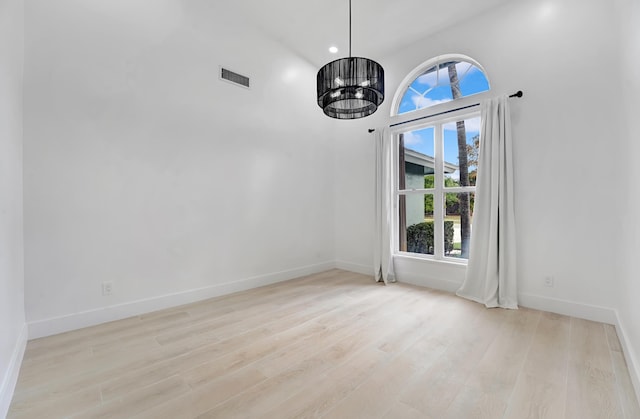 spare room with light hardwood / wood-style floors, a high ceiling, and a chandelier