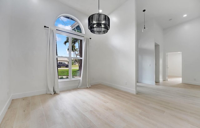 unfurnished dining area with a towering ceiling, light hardwood / wood-style floors, and an inviting chandelier