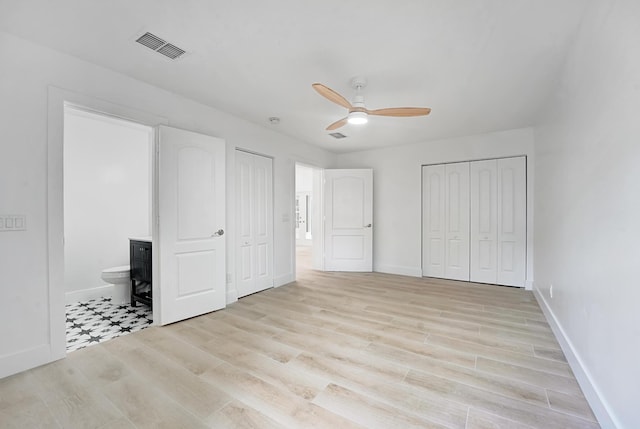 unfurnished bedroom featuring ensuite bath, ceiling fan, multiple closets, and light wood-type flooring